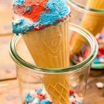 Glass jar holding a cone with red white and blue ice cream with sprinkles in the bottom of jar.