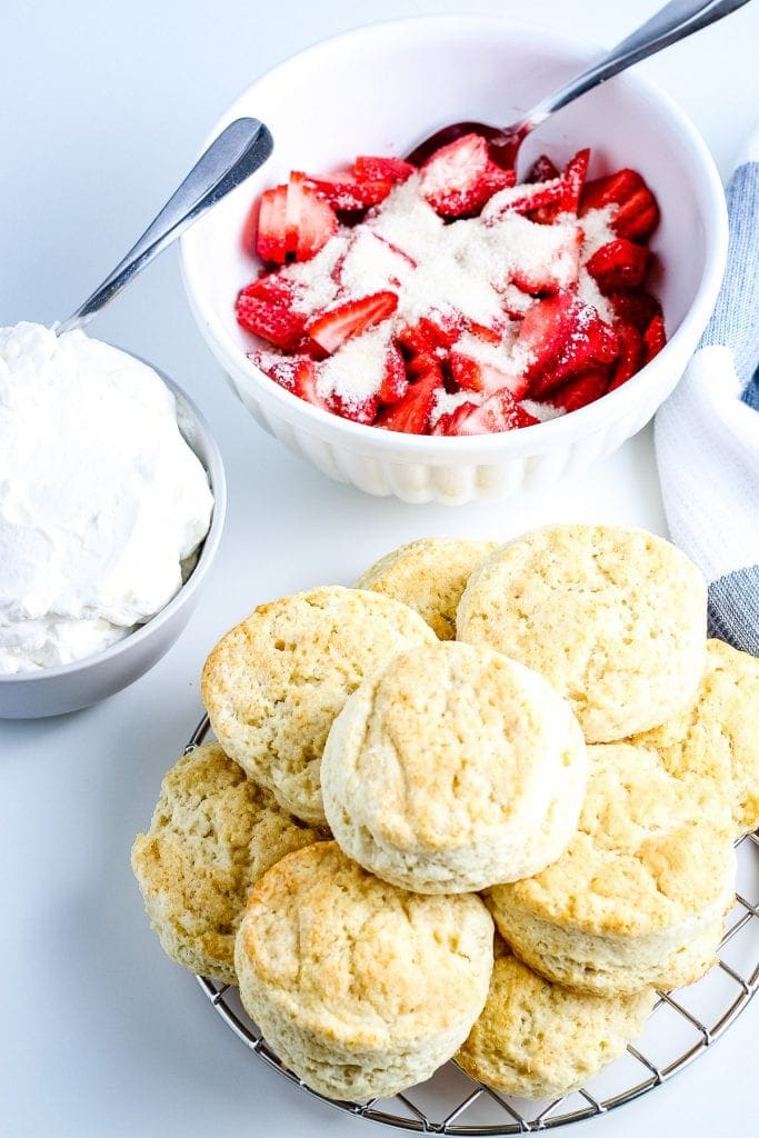 Image showing homemade biscuits on a plate, strawberries with sugar in a bowl and homemade whipped cream in seperate bowl.