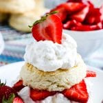 A strawberry shortcake on white plate with strawberries in background and biscuits.