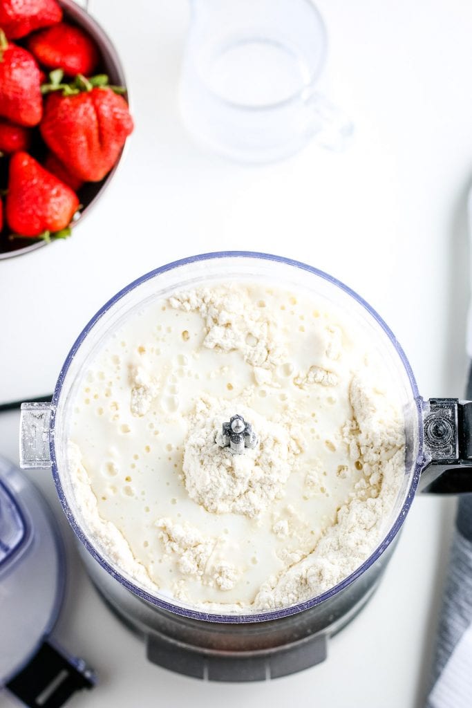 Food processor with milk being added to biscuit dough.