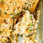 Glass baking dish full of tuna casserole being scooped with a wooden spoon