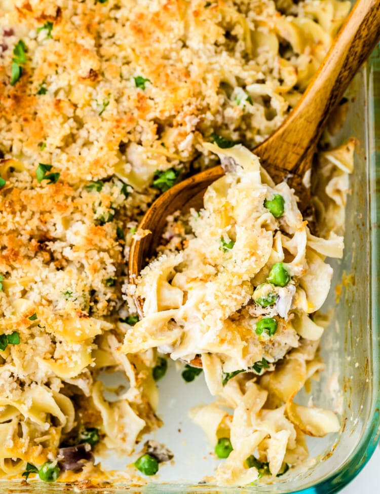 Glass baking dish full of tuna casserole being scooped with a wooden spoon