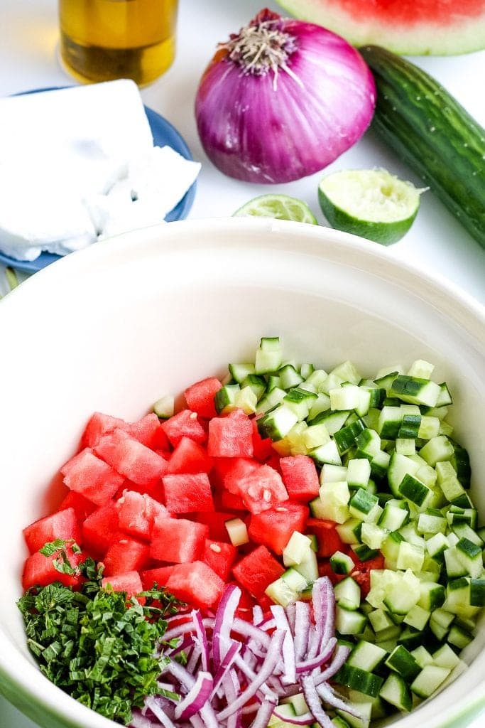 Bowl of ingredients for watermelon salad before being mixed. Ingredients included diced watermelon cucumbers, red onion and mint.