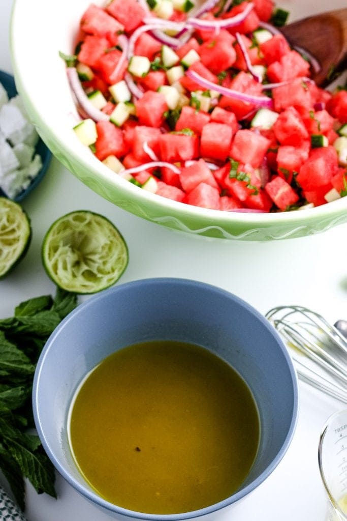 Blue bowl with mixed lime dressing a bowl of watermelon salad in a bowl in the background