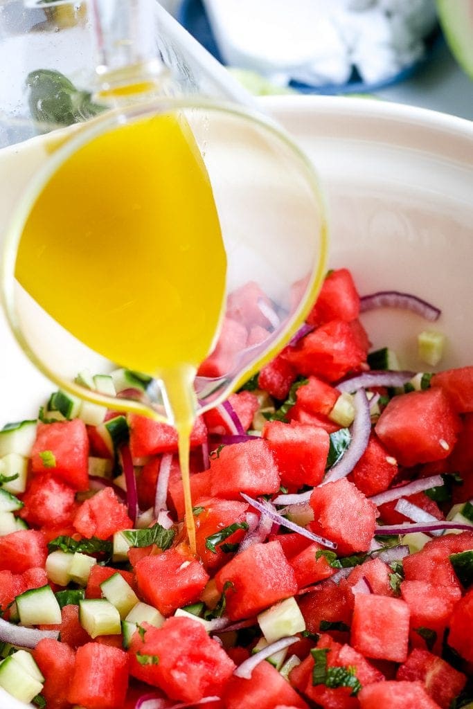 Lime Dressing being poured out of measuring cup into bowl of watermelon salad