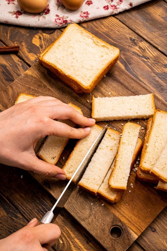 hand holding slice of bread and other hand holding knife slice bread into strips