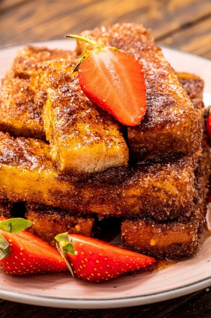 Close up of Air Fryer French Toast sticks topped with a sliced strawberry and more sliced strawberries next to it on the plate