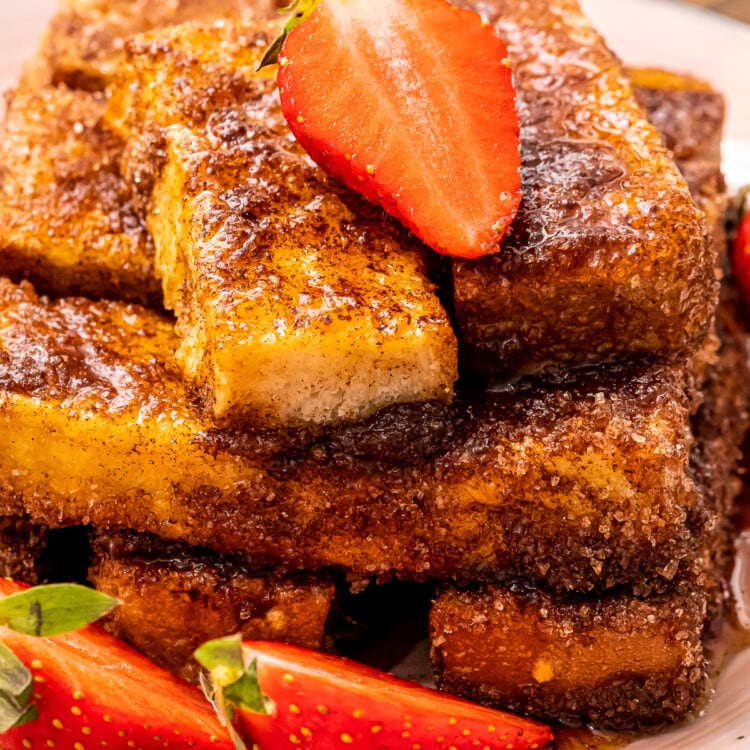 Close up of Air Fryer French Toast sticks topped with a sliced strawberry and more sliced strawberries next to it on the plate