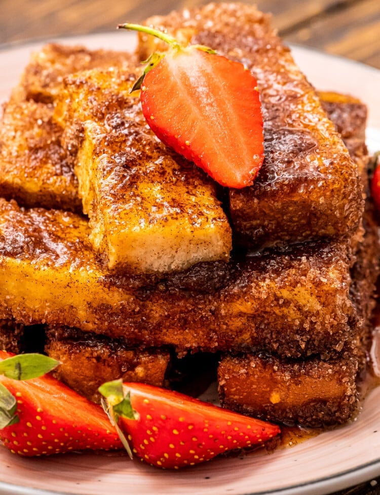 Close up of Air Fryer French Toast sticks topped with a sliced strawberry and more sliced strawberries next to it on the plate