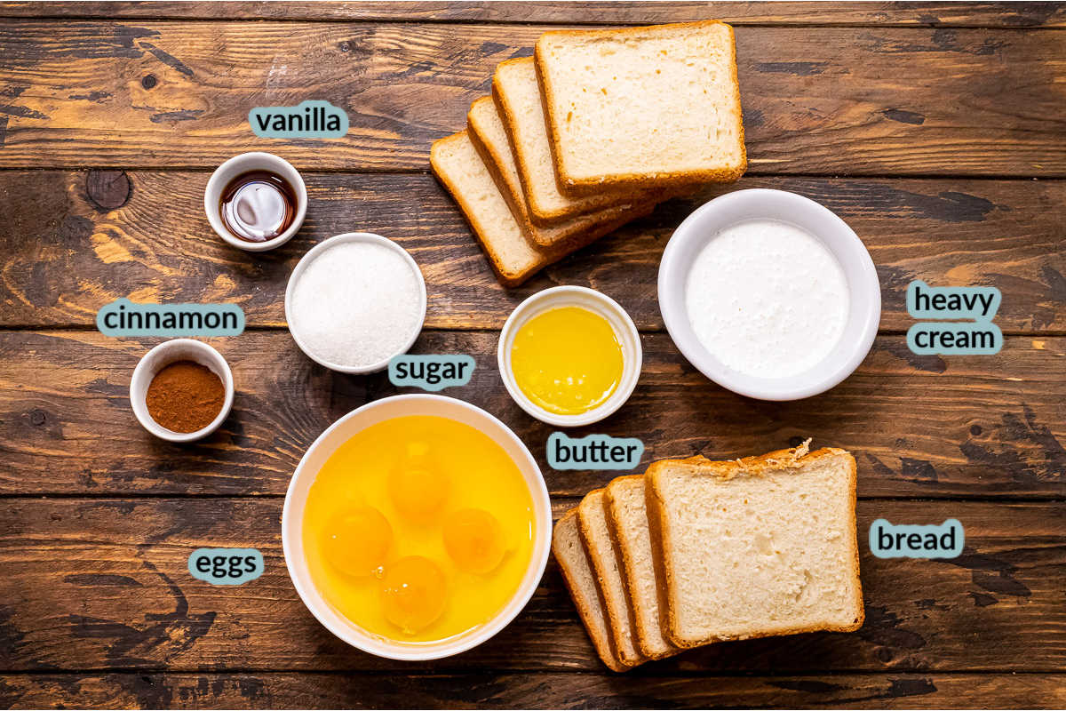 Ingredients for French Toast Sticks on a wood background including bread slices along with bowls of eggs butter sugar vanilla cinnamon