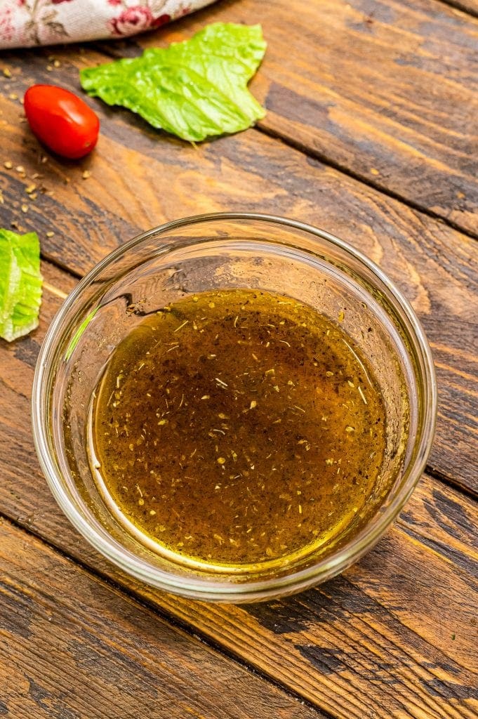 Mixed oil dressing for salad in glass bowl on wooden background