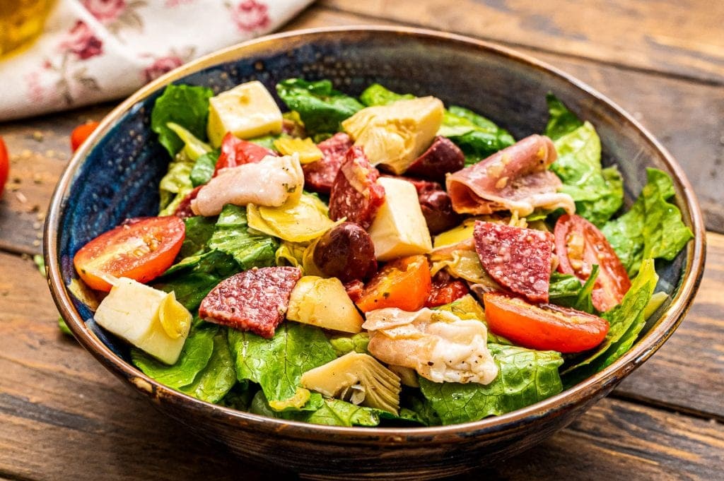 Dark blue ceramic bowl with tossed Antipasto Salad in it.