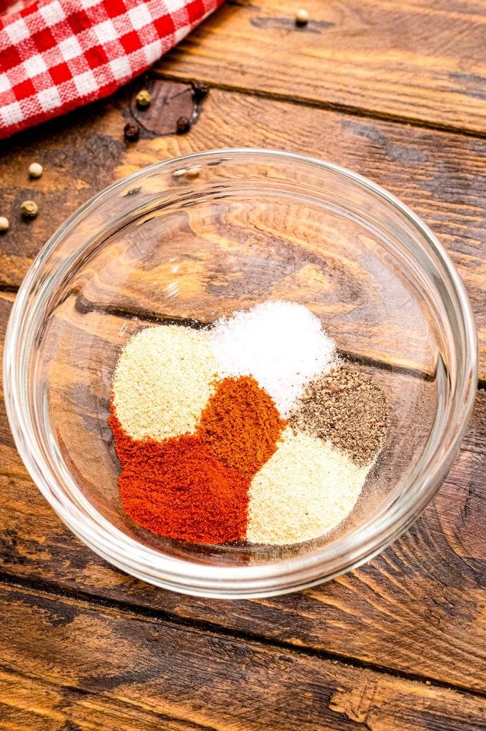 Small glass bowl sitting on wooden background full of spices before mixing together.