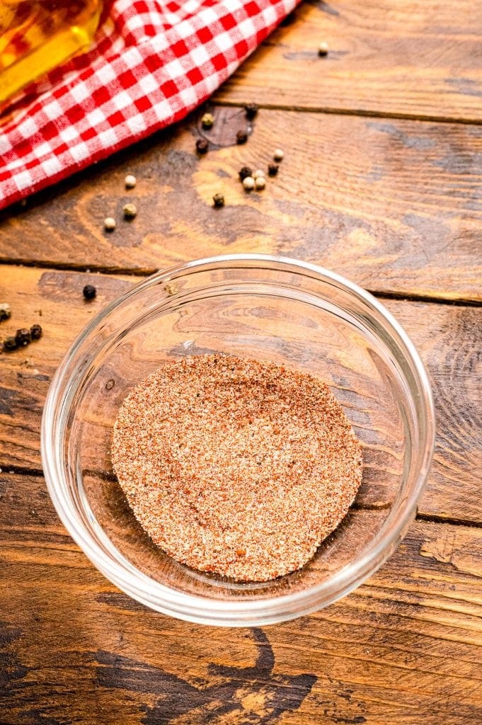 Small glass bowl sitting on wooden background full of spices after mixing together.