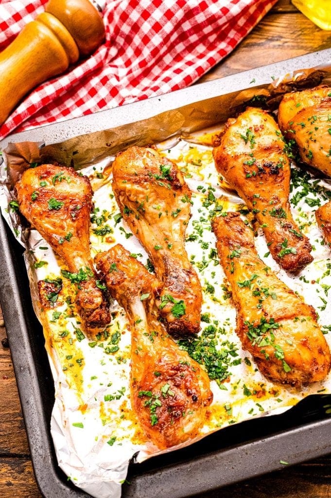 Baked Chicken Legs on an aluminum foil lined pan after baking and garnished with chopped parsley.