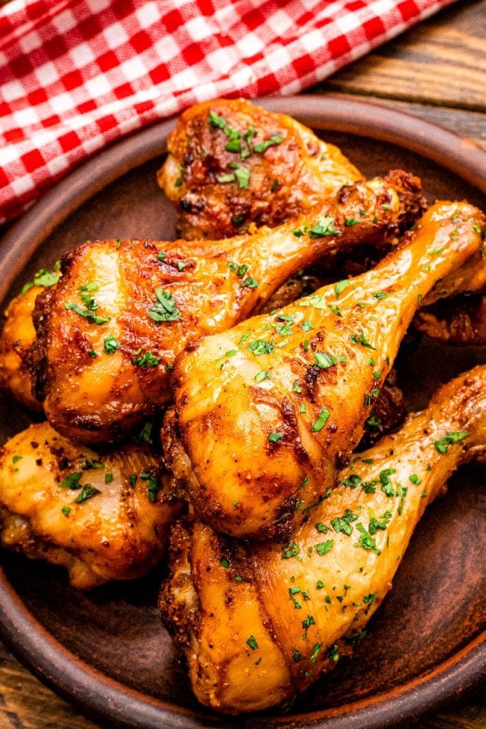 Stack of chicken drumsticks on wooden plate garnished with chopped parsley.