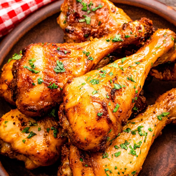 Stack of chicken drumsticks on wooden plate garnished with chopped parsley.