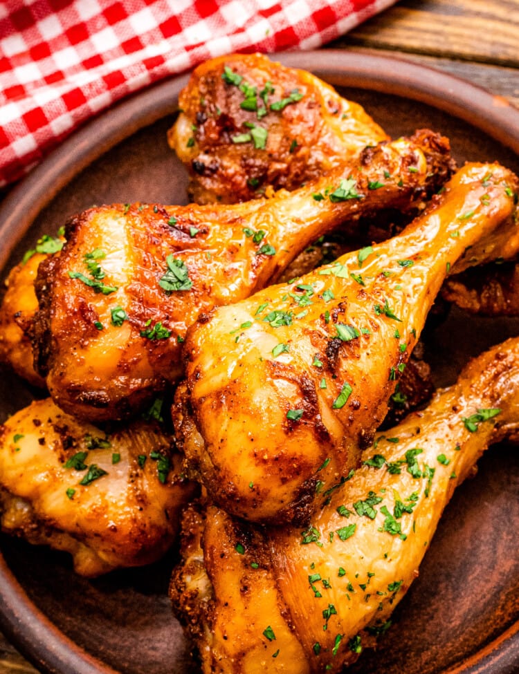 Stack of chicken drumsticks on wooden plate garnished with chopped parsley.