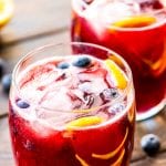 Two glasses on wooden background of freshly made blueberry lemonade with ice, blueberries, and lemon slices in glasses.