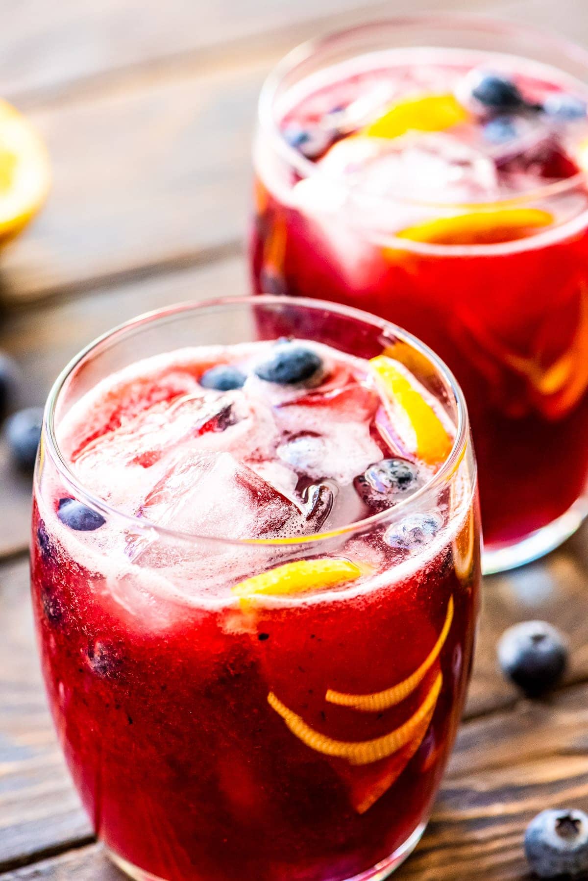 Two glasses on wooden background of freshly made blueberry lemonade with ice, blueberries, and lemon slices in glasses.