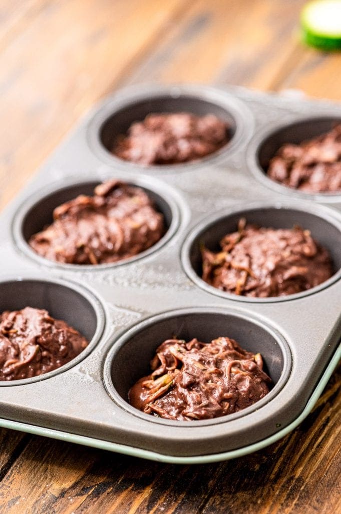 Muffin tin with batter in it on wooden background.