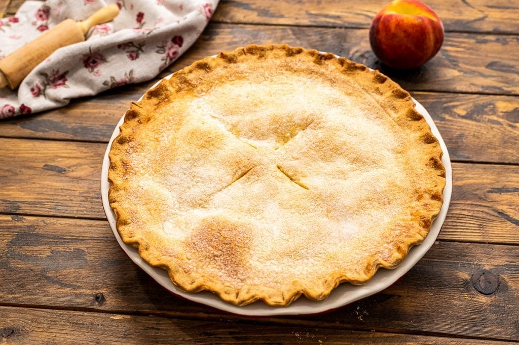 Double Crust Peach Pie Baked in pie dish on wooden background