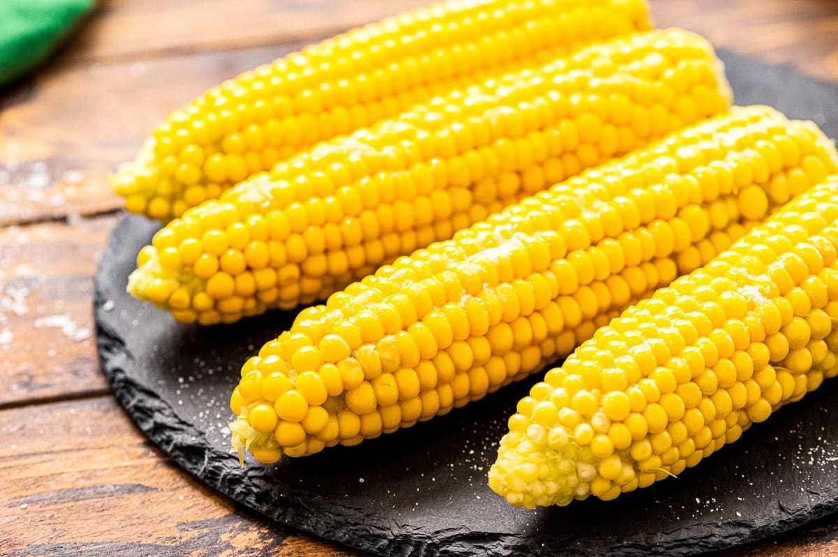 Four pieces of corn on the cob on a slate round board.