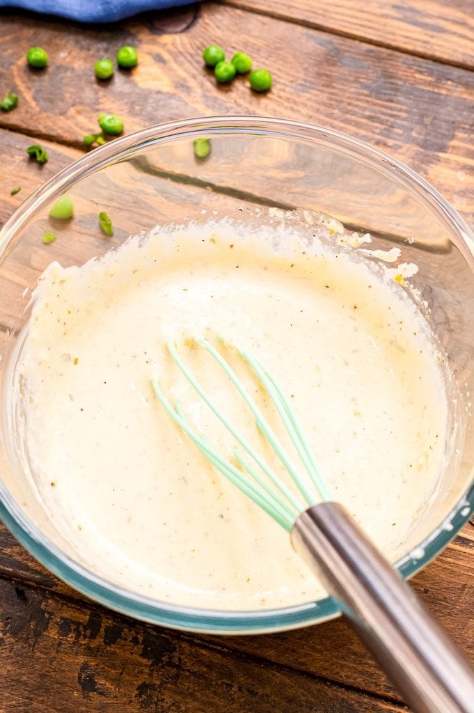 Salad dressing mixed together with whisk sitting in glass bowl.