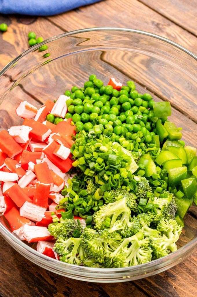 Glass bowl showing green peppers, broccoli, imitation crab meat and peas.