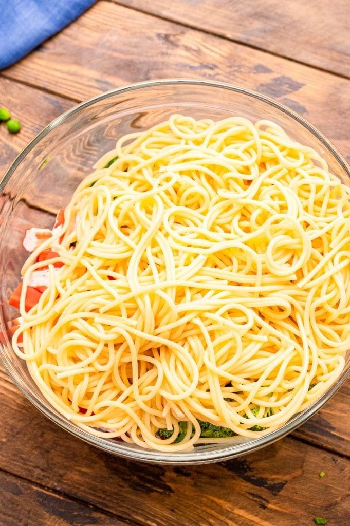 Cooked spaghetti noodles in glass bowl over the top of other salad ingredients.