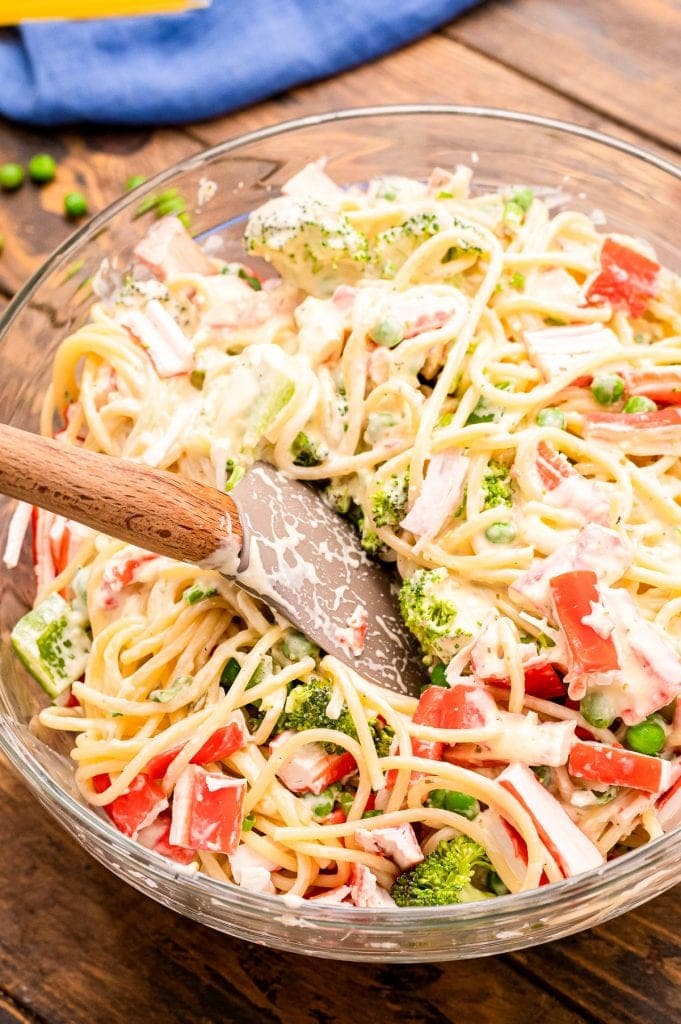 Spatula mixing salad ingredients together in glass bowl.