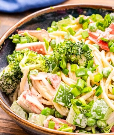 Close up image showing half of a bowl of crab pasta salad with spagheti noodles, creamy dressing, green onions, imitation crab meat etc.