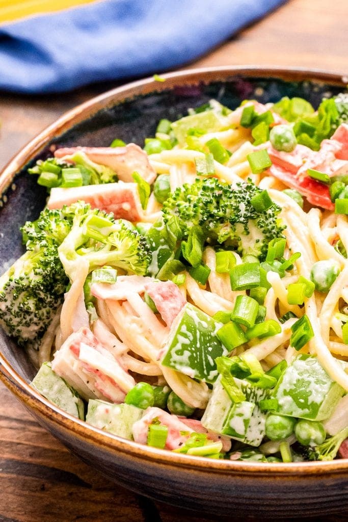 Close up image showing half of a bowl of crab pasta salad with spagheti noodles, creamy dressing, green onions, imitation crab meat etc.