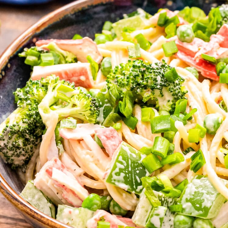 Close up image showing half of a bowl of crab pasta salad with spagheti noodles, creamy dressing, green onions, imitation crab meat etc.