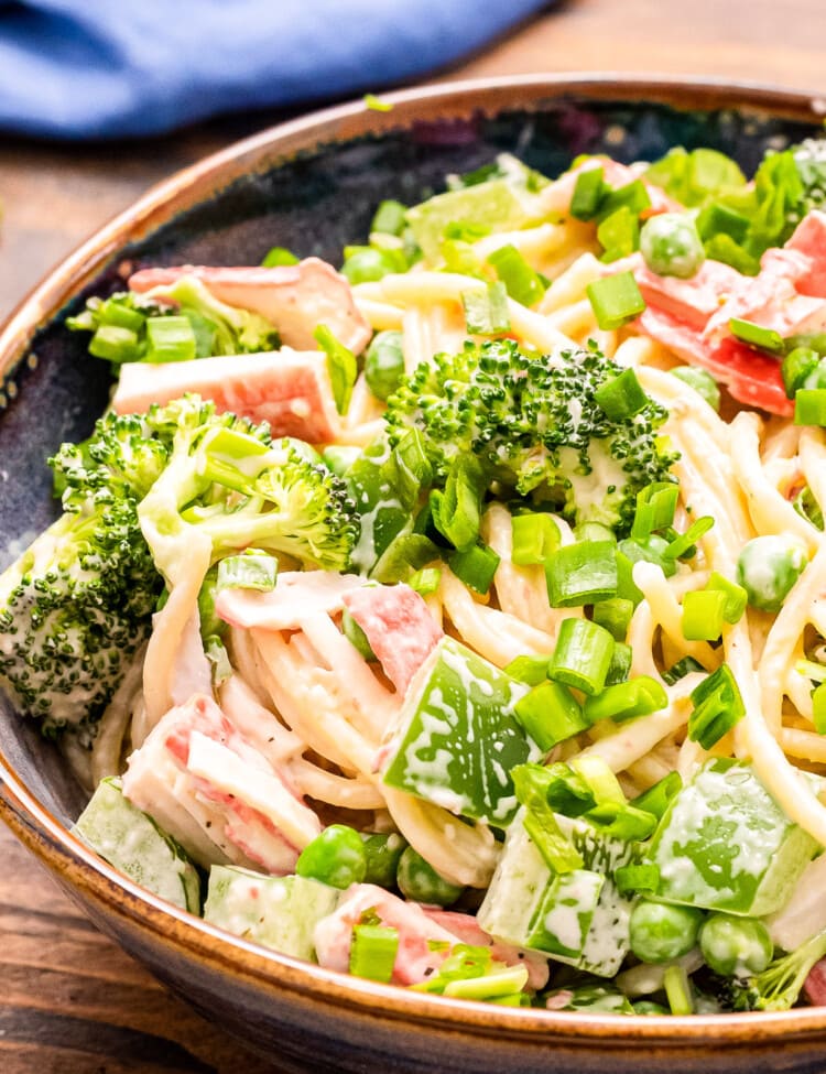 Close up image showing half of a bowl of crab pasta salad with spagheti noodles, creamy dressing, green onions, imitation crab meat etc.