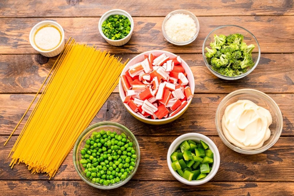 Overhead image showing ingredients for salad like spaghetti noodles, green onions, peas, broccoli, mayonnaise, etc.