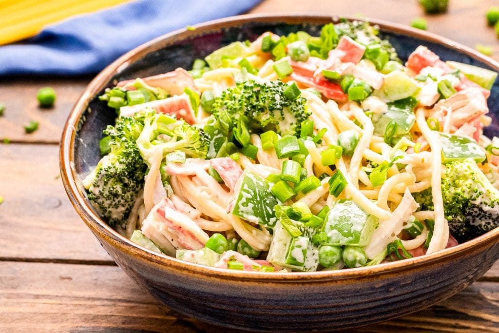 A landscape photo featuring prepared crab pasta salad in a clay bowl with a blue napkin folded up in background.