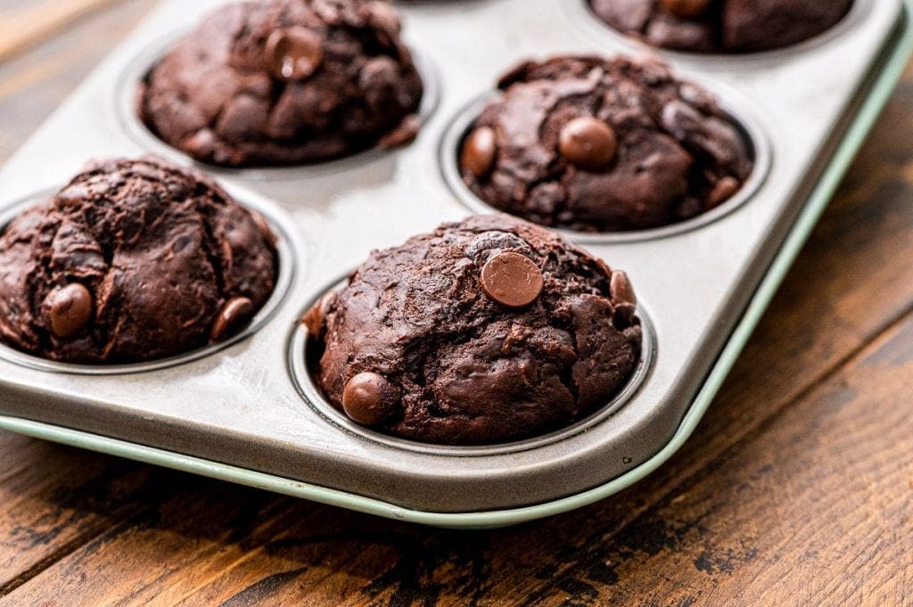 Muffin tin with with chocolate zucchini muffins in it on wooden background