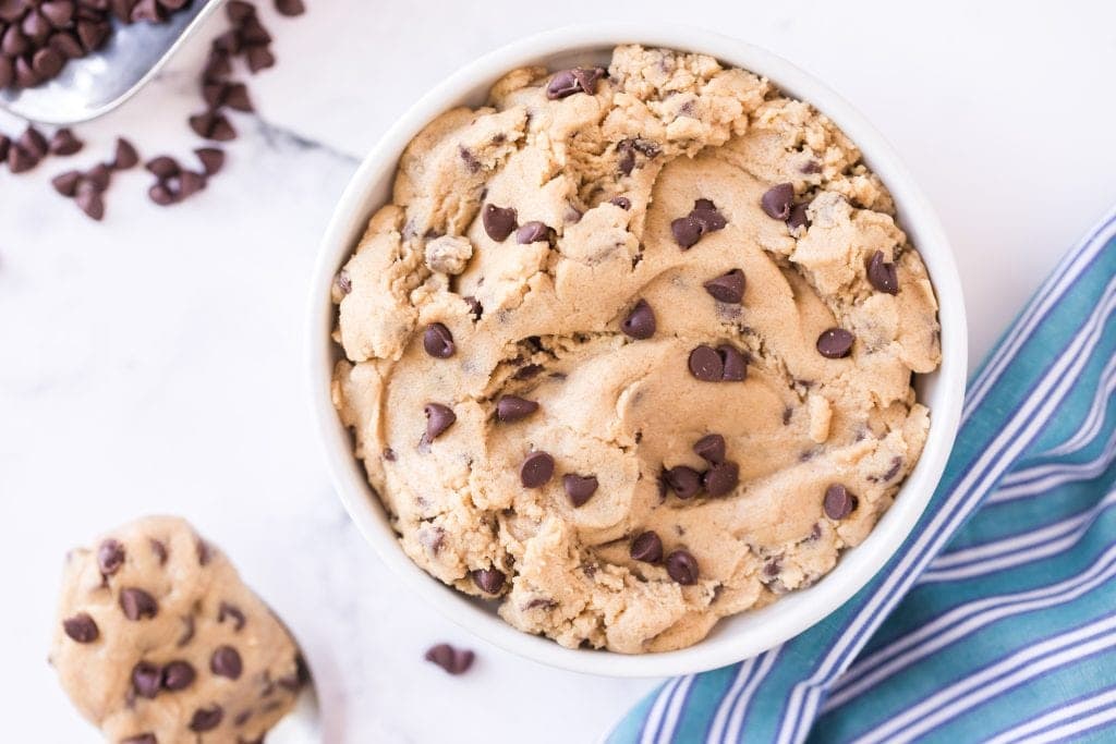 Overhead image of Edible Chocolate Chip Cookie Dough in white bowl. A spoon with it on next to it. Blue striped napkin in background