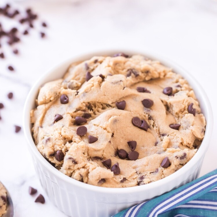 White bowl full of edible cookie dough. Blue napkin and chocolate chips beside it.