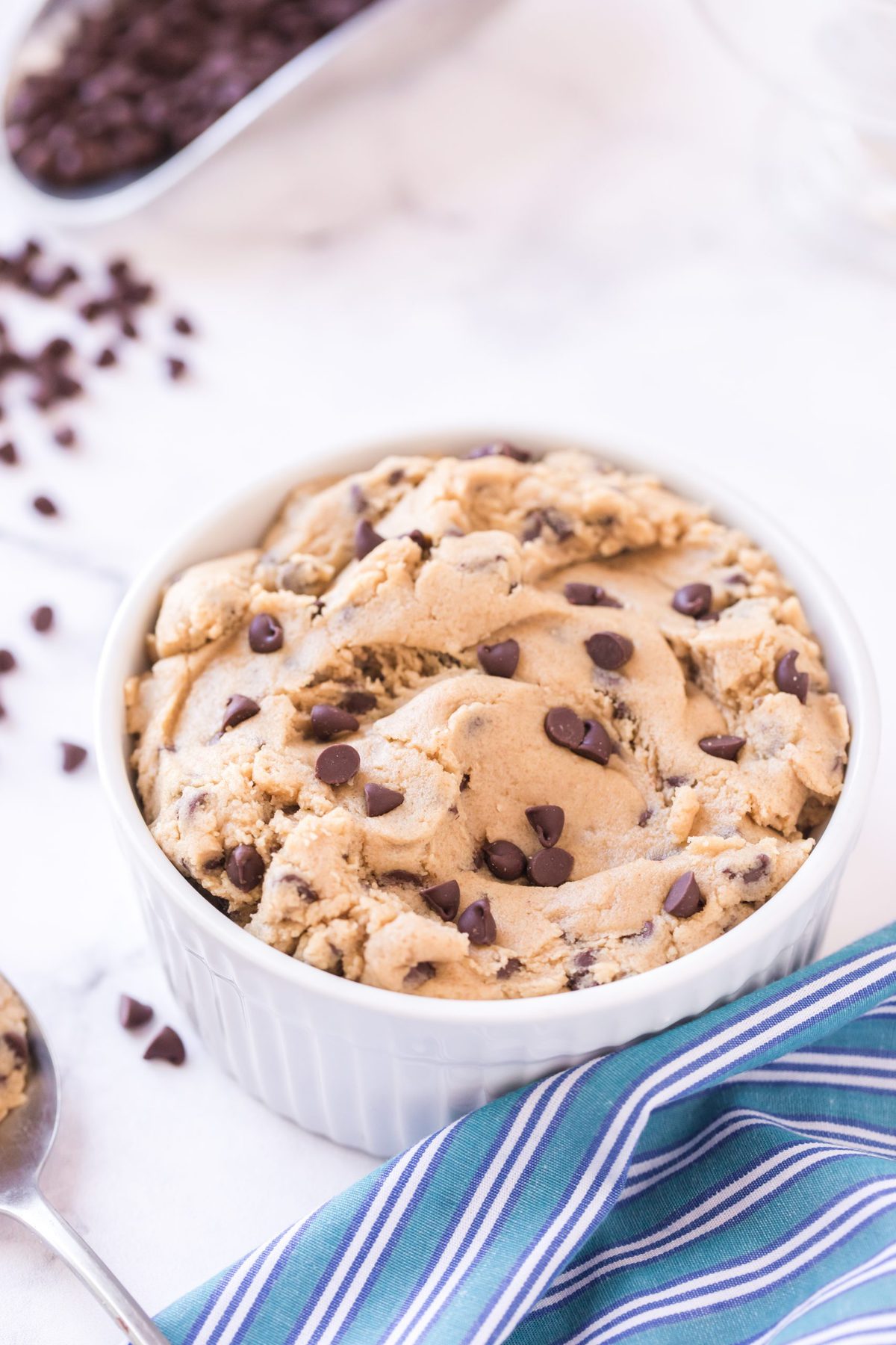 White bowl full of edible cookie dough. Blue napkin and chocolate chips beside it.