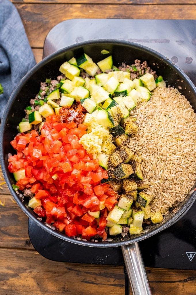 Skillet with chopped tomatoes, zucchini and dry brown rice before cooking
