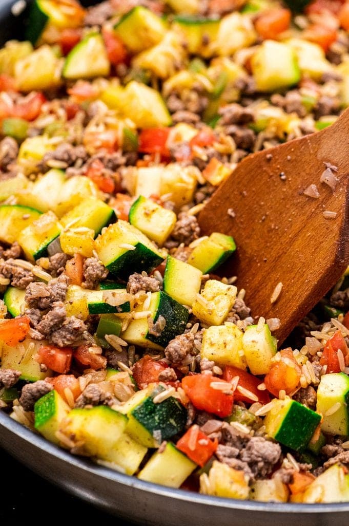 Wooden Spoon stirring ground beef and zucchini mixture.