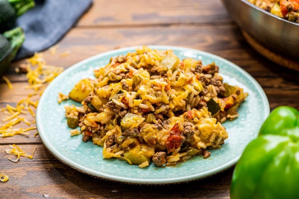 Light blue plate with a serving of ground beef and zucchini skillet on it that's topped with melted cheese.