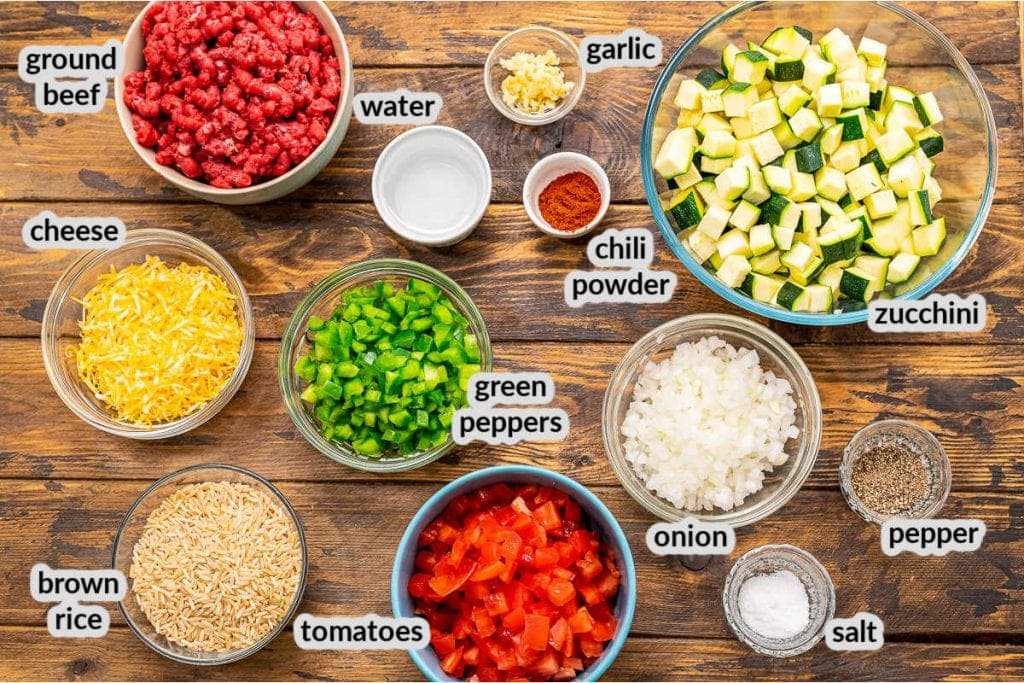 Overhead image showing ingredients in bowls for hamburger and zucchini skillet on wooden background