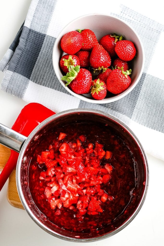 Strawberry sauce in saucepan with fresh diced strawberries added to it.