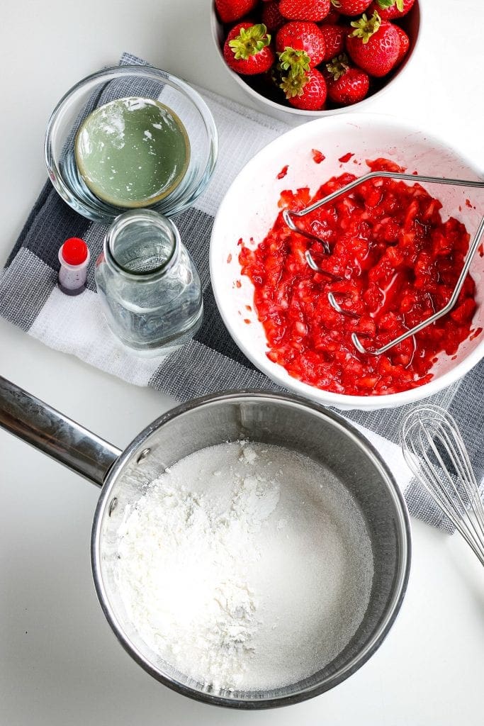 Metal bowl with sugar and cornstarch along with the rest of the ingredients in background for strawberry sauce.