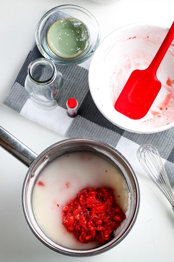 Metal bowl with sugar mixture and mashed strawberries added to it.