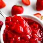 Spoon with a scoop of strawberry sauce on it with more in a bowl in background