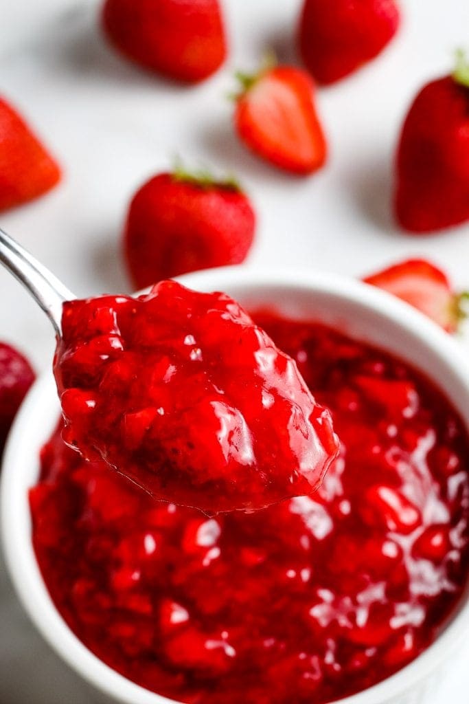 Spoon with a scoop of strawberry sauce on it with more in a bowl in background